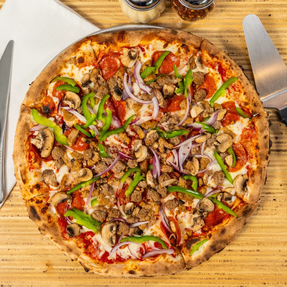 Overhead view of a Bear Brick Oven Co. pizza with pepperoni, sausage, mushrooms, green peppers, and red onions.