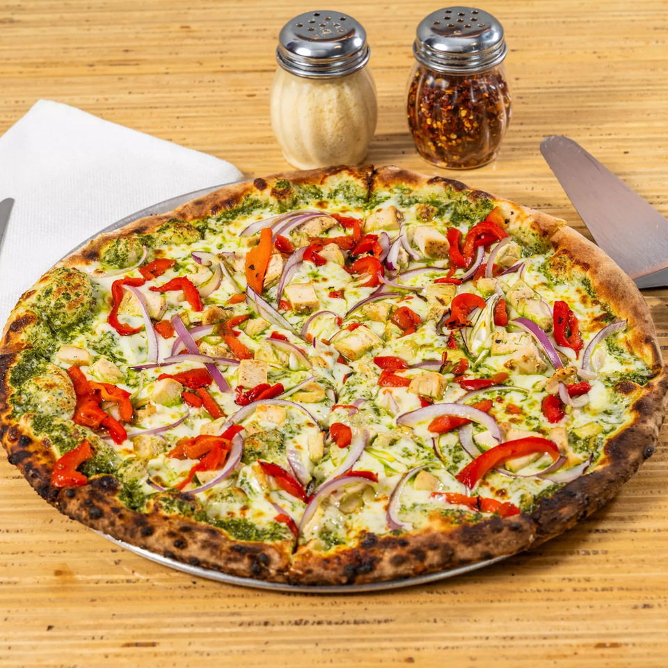 Bear Brick Oven Co. pesto chicken pizza with red peppers and red onions on a wooden table.