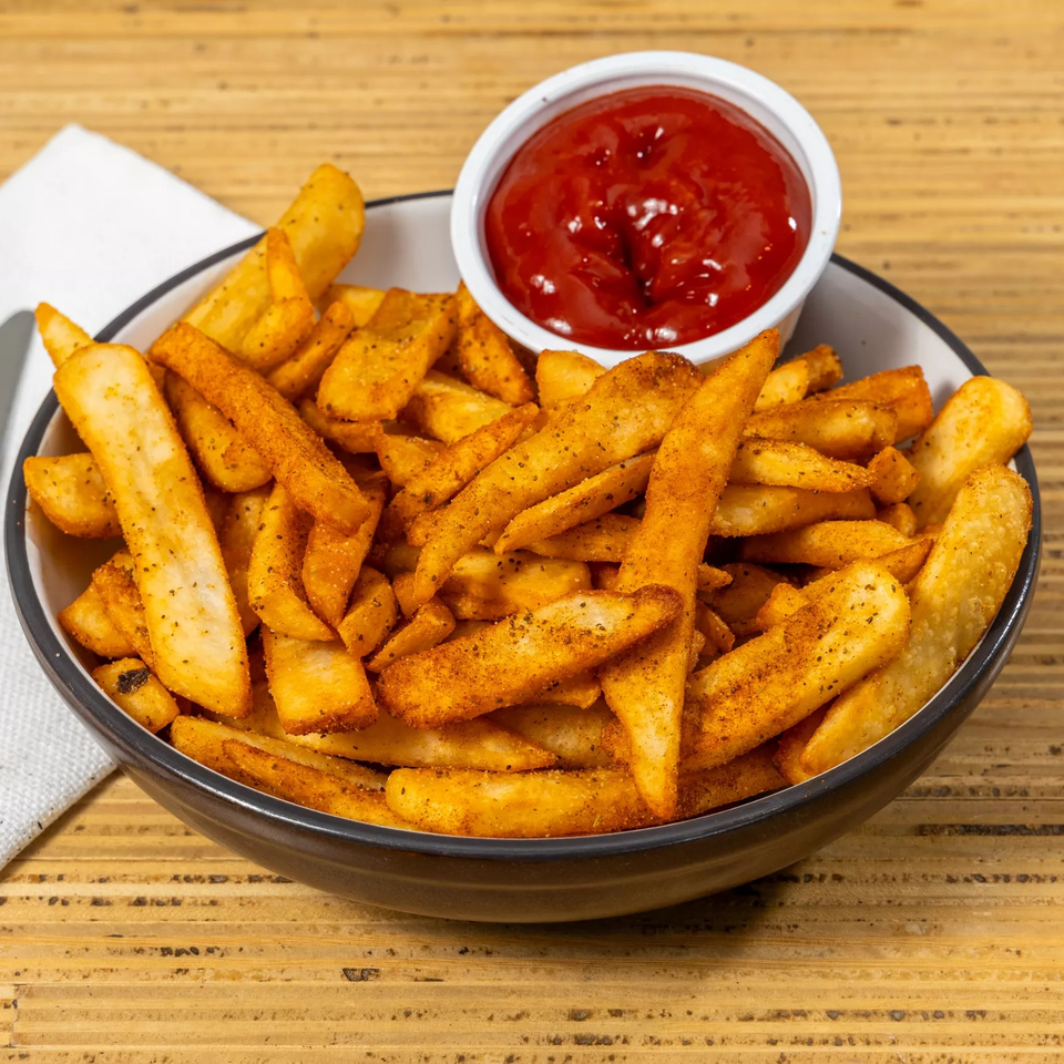 A bowl of seasoned Bear Brick Oven Co. fries with a side of ketchup on a wooden table.
