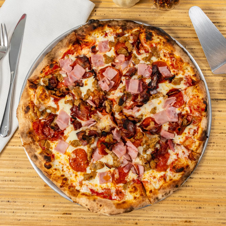 A whole meat lover's pizza with pepperoni, ham, and sausage on a wooden table.
